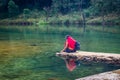 Isolated girl sitting near calm river surrounded by dense green forests with refection at morning Royalty Free Stock Photo