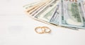 Isolated golden wedding rings and banknotes dollars, on a white wooden background, copy space. Royalty Free Stock Photo