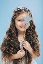 Isolated image of satisfied beautiful curly woman with blue eyes, covers face with magic wand, has long curly hair, poses over