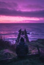 An isolated man sits on the grassy hillside overlooking an old broken pier Royalty Free Stock Photo