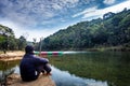 Isolated man sitting near calm river surrounded by dense green forests and blue sky with refection Royalty Free Stock Photo