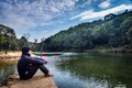 Isolated man sitting near calm river surrounded by dense green forests and blue sky with refection Royalty Free Stock Photo
