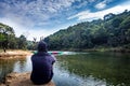 Isolated man sitting near calm river surrounded by dense green forests and blue sky with refection Royalty Free Stock Photo