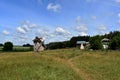 An abandoned wooden windmill in the vast green field near the forest. Barns and other constructions stand next