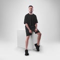 Isolated mockup of trendy black men`s oversized t-shirt with shorts on man sitting on cube