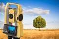 Isolated oak tree in a golden wheat field and 3D rendering of a geodesic device, called Total Station used for the survey of Royalty Free Stock Photo