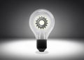 Isolated object shot of a light bulb with cog wheel gear inside on a dark background Royalty Free Stock Photo