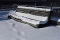 Isolated old wooden bench under a layer of snow in a snow-covered winter background. Sunny cold day. Royalty Free Stock Photo