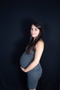 Isolated portrait of beautiful smiling woman in dress waiting for baby in black background Royalty Free Stock Photo