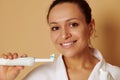 Isolated portrait on beige background of an attractive woman with beautiful toothy smile holding a toothbrush with toothpaste near Royalty Free Stock Photo