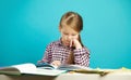 Isolated portrait of girl on blue background, sitting at desk, reading the book carefully with his hand to the chin Royalty Free Stock Photo