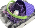 Isolated purple polka dot basket pail with decorated Easter egg is sitting on an egg carton.