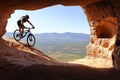 ISOLATED RIDER WITH HELMET AND BACKPACK DESCENDING IN A MOUNTAIN BIKE TOWARDS THE ENTRANCE OF A CAVE IN SUMMER