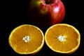 Isolated ripe orange fruit cut in half with shiny red apple. Black background. Royalty Free Stock Photo