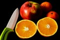 Isolated ripe orange fruit cut in half. red apple and small tangerines. White porcelain knife blade. Black background. Royalty Free Stock Photo
