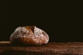 Isolated rustic and golden round loaf of fresh whole grain bread on dark black background on top of wooden kitchen table Royalty Free Stock Photo