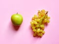 Isolated set of a green apple with a bunch of sweet seedless grapes in studio with millennial pink background