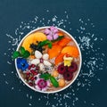 Isolated shot of bowl with tropical fruit decorated with flowers, mint, coconut flakes isolated over dark blue background. Fresh