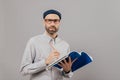 Isolated shot of self confident male author creats new novel, holds pencil and notepad, writes down notes and ideas, wears optical