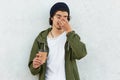 Isolated shot of sleepy curly man keeps hand on nose, dressed in stylish hat and anorak, holds takeout coffee, wants to have rest