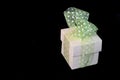 Isolated single gift box with green ribbon with white spots on black background