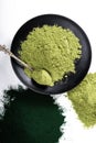 An isolated tablespoon of dried organic wheat grass and spirulina powder, on white rustic background