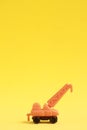 Isolated vertical closeup shot of an orange crane toy on a yellow table