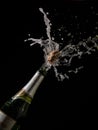 Isolated vertical shot of an opened champagne bottle with the cork in the air on a black background