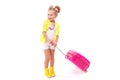 Pretty little girl in yellow shirt, white shorts and boots hold pink suitcase by the handle Royalty Free Stock Photo