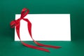 White gift card with red ribbon bow on deep green background. Royalty Free Stock Photo