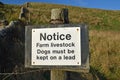 Isolated white sign with blurred stone wall, grass and blue sky background. Text Notice Farm Livestock Dogs Must be Kept on a Lead Royalty Free Stock Photo