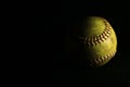 Isolated yellow softball with red seams on a black background. Royalty Free Stock Photo