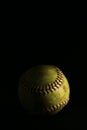 Isolated yellow softball with red seams on a black background. Royalty Free Stock Photo