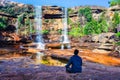 Isolated young man meditating near waterfall falling from mountain top with reflection and blue sky Royalty Free Stock Photo