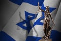 Israel flag with statue of lady justice and judicial scales in dark room. Concept of judgement and punishment