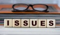 ISSUES - word on wooden cubes on the background of a folder with documents and glasses