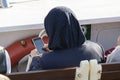 Woman in headscarf is dealing with mobile phone. The photo was taken on the ferry and sunny outdoors