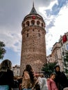Many tourists at the foot of the Galata Tower, vertical. People look at the ancient landmark