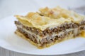 Italian beef lasagne on a white round plate, white wooden background.