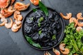 Italian black ravioli with seafood shrimps and crabs on black plate, gray stone slate background. Top view