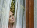 Italian blonde woman forced into house by quarantine due to coronavirus covid-19, looks at the outside world from the window Royalty Free Stock Photo