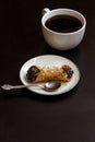 Italian cannoli with chocolate chips on white plate and coffee cup on black background