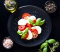 Italian caprese salad with sliced tomatoes, mozzarella cheese, basil, olive oil on black plate over dark wood background with Royalty Free Stock Photo