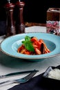 Italian cuisine. Pasta with seafood, tomatoes and cheese in a blue, a fork and a knife on a light background. Royalty Free Stock Photo