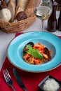 Italian cuisine. Pasta with seafood, tomatoes and cheese in a blue, a fork and a knife on a light background. Royalty Free Stock Photo