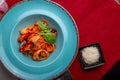 Italian cuisine. Pasta with seafood, tomatoes and cheese in a blue, a fork and a knife on a light background. Royalty Free Stock Photo