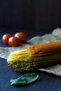 Italian Cuisine. raw spaghetti, red cherry tomatoes and green leaves with sackcloth on a wooden table Royalty Free Stock Photo