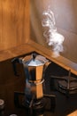 An Italian espresso mokka machine with steam getting out of it while making a fresh coffee in a regular kitchen with wood and ston