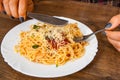 Woman hand holding fork and knife with spaghetti bolognese in white plate on wooden table. Royalty Free Stock Photo