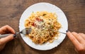 Woman hand holding fork and knife with spaghetti bolognese in white plate on wooden table. top view Royalty Free Stock Photo